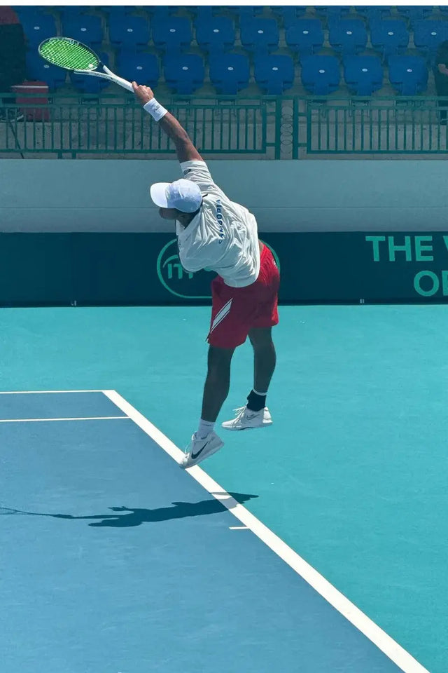Player follows through on a serve, gripping the racket on a blue court.