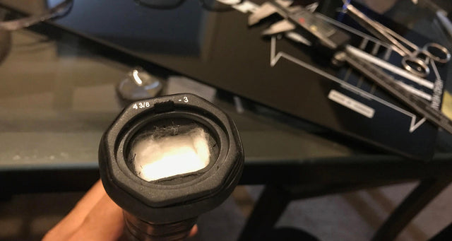 Tennis racket handle end showing 4 3/8 grip size, with calipers and tools nearby.