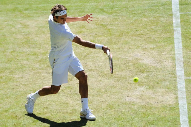 Roger Federer in white attire hitting a forehand on a Wimbledon grass court.