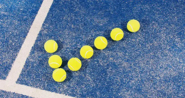 Tennis balls arranged in a checkmark shape on a blue court near the baseline.