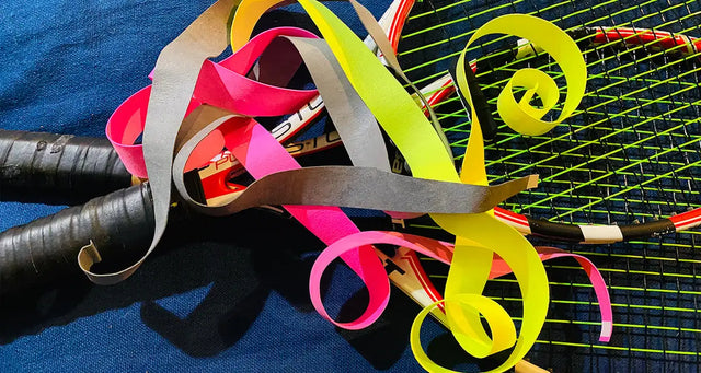 Colorful tennis overgrips curling over rackets on a blue cloth background.