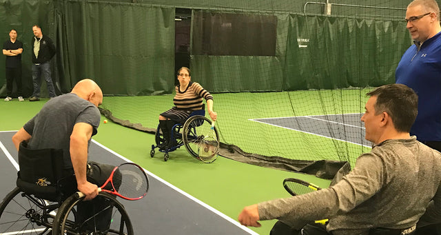 Wheelchair tennis players holding rackets during an indoor beginner practice session on court.