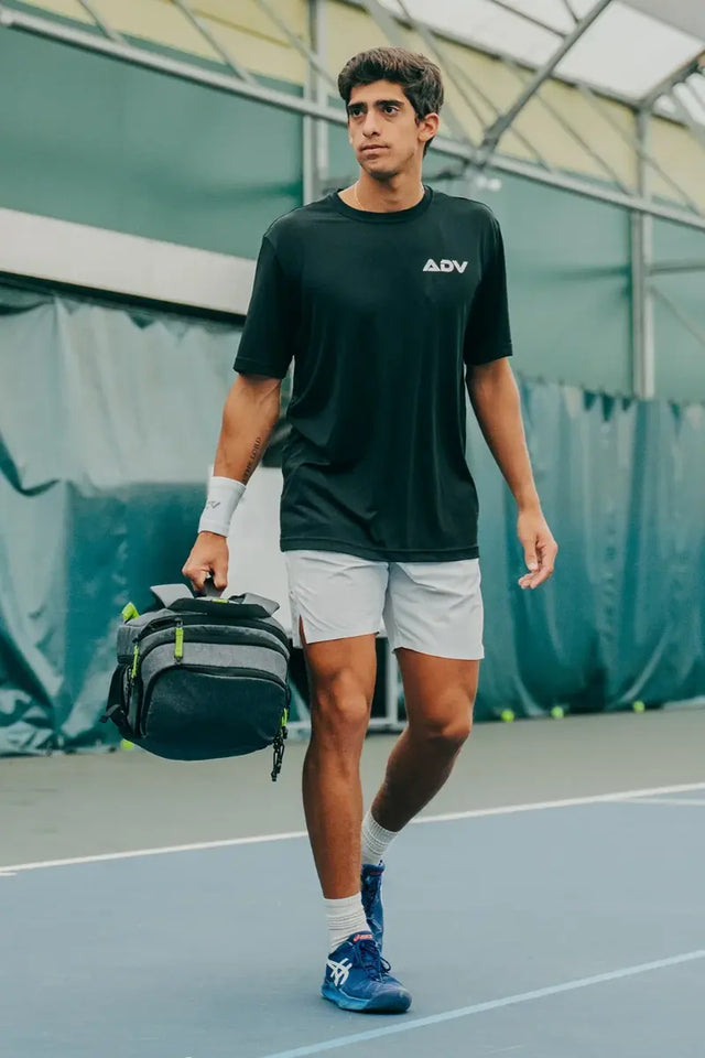professional tennis bag with multiple compartments and a sleek gray design, carried by a male player walking on an indoor court.