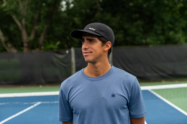 Person wearing black ADV lightweight tennis cap on a blue tennis court.
