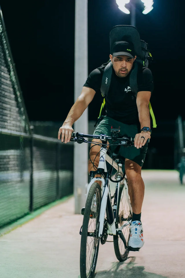 Cyclist wearing the black ADV Tennis Backpack V2 with neon accents riding at night.