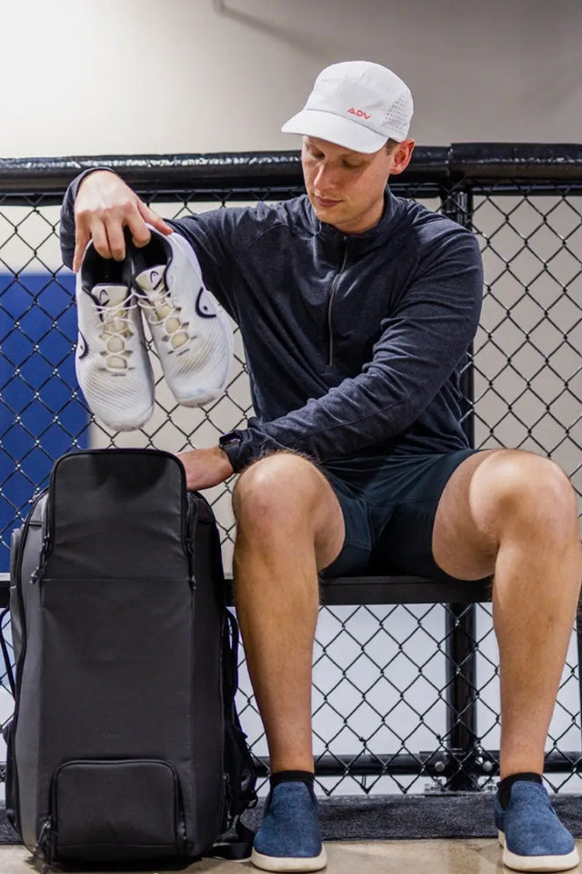 Tennis backpack being packed with shoes by athlete on a bench inside a training facility