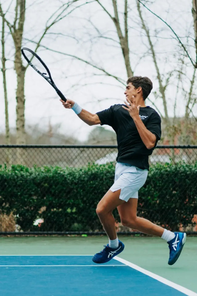 A tennis player swings his racket mid-air, highlighting the benefits of tennis dampeners for reducing string vibrations.