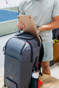 Person loading a laptop into a grey ADV pickleball backpack at a court.