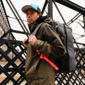 Person wearing grey RPM Pickleball Bag Pro backpack with red strap on urban bridge.