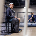 Black RPM Pickleball Bag Pro resting beside a seated player at an indoor court.