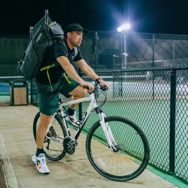 Pro tennis bag worn by cyclist outside court, designed for carrying multiple rackets and gear with ease and comfort.