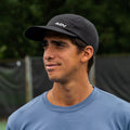 Person wearing black ADVantage tennis cap with perforated panels on an outdoor court.