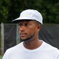 Person wearing white perforated ADVantage tennis cap with green logo on a court.