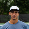 Player wearing white ADVantage tennis cap with red logo on an outdoor court.
