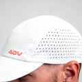 White ADVantage tennis cap with orange logo and laser-cut side ventilation, worn on-model.