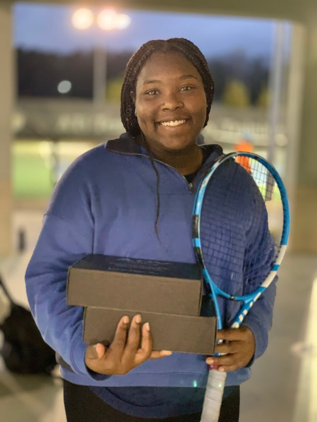 Tennis racket and tournament tennis bag accessories held by a smiling player on an indoor court.