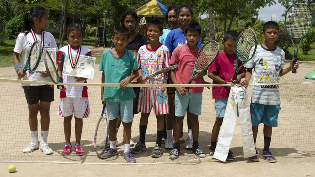 Tennis racket backpack and gear displayed behind a group of children posing on a clay tennis court.