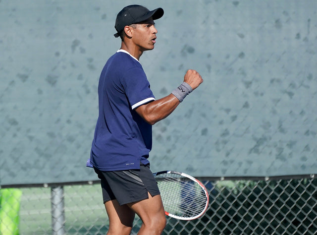 Tennis player holding a tennis racket celebrates on the court wearing a gray ADV Tennis Wristbands during a match