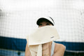 Player wipes face with cream ADV court towel by a tennis net.