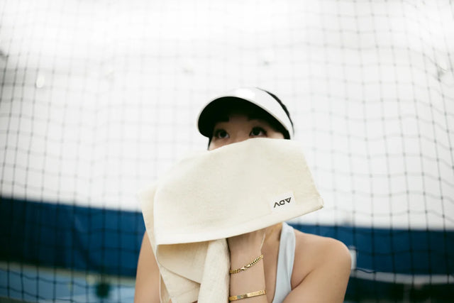 Player wipes face with cream ADV court towel by a tennis net.