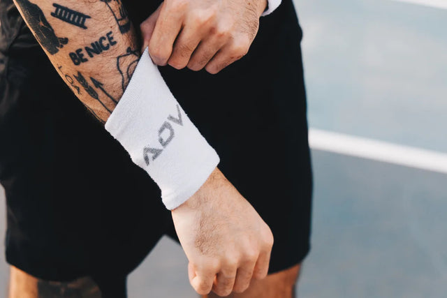 White ADV tennis wristband worn on a player's forearm beside a blue court.